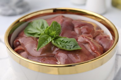 Photo of Bowl with raw chicken liver and basil on table, closeup