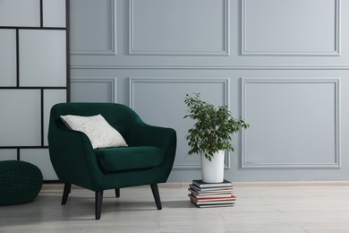 Photo of Stylish armchair with pillow and houseplant on floor near light grey wall indoors, space for text. Interior design