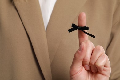 Woman in beige suit showing index finger with tied black bow as reminder, closeup