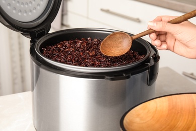 Photo of Woman taking delicious brown rice from multi cooker indoors, closeup