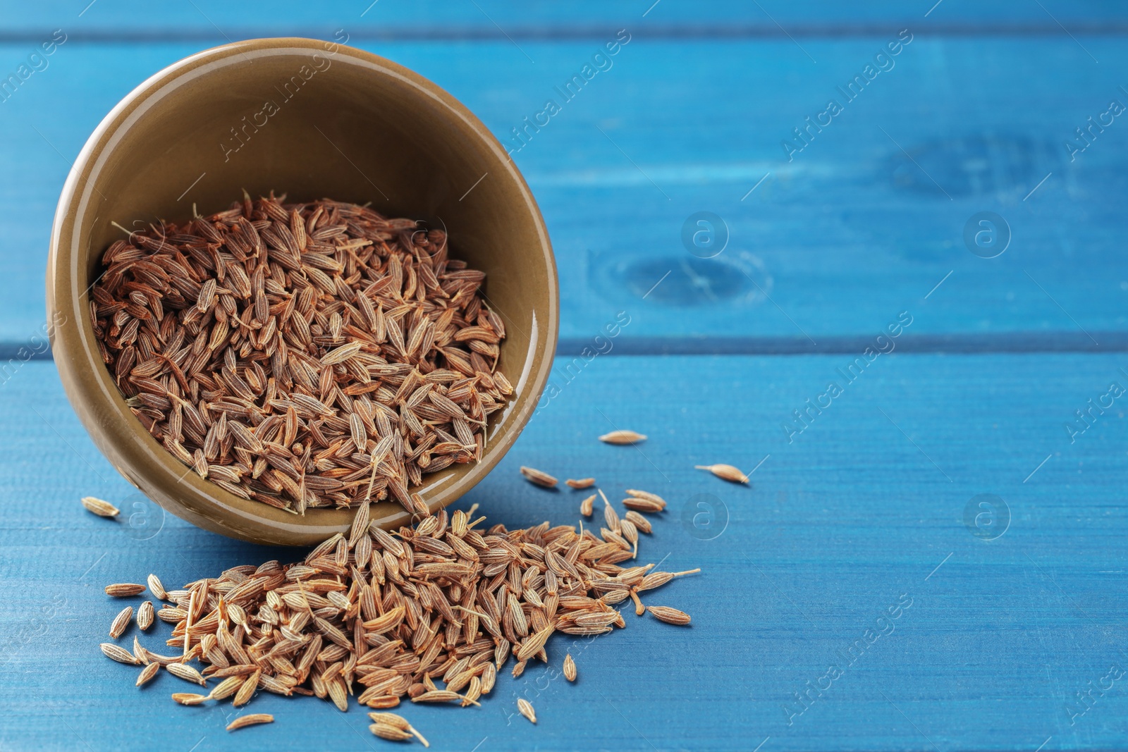 Photo of Overturned bowl with caraway seeds on blue wooden table, space for text