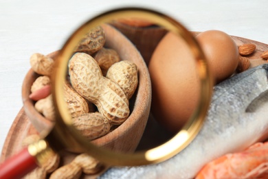 Different products with magnifier focused on peanuts and eggs, closeup. Food allergy concept