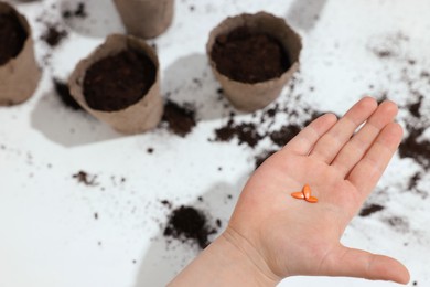 Photo of Little girl holding vegetable seeds at white table, closeup. Space for text