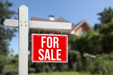 Image of Sale sign near beautiful house outdoors. Red signboard with words