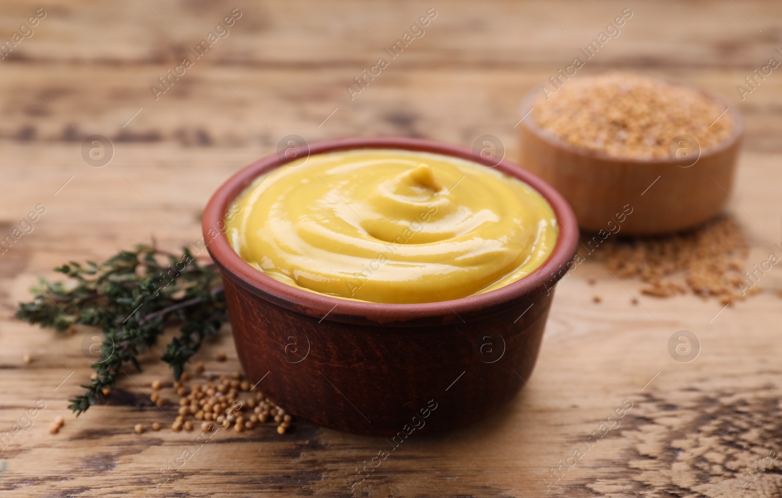 Photo of Delicious mustard, seeds and thyme on wooden table, closeup