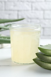 Photo of Fresh aloe juice in jar and leaves on white marble table, closeup