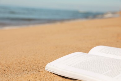 Open book on sandy beach near sea, closeup. Space for text