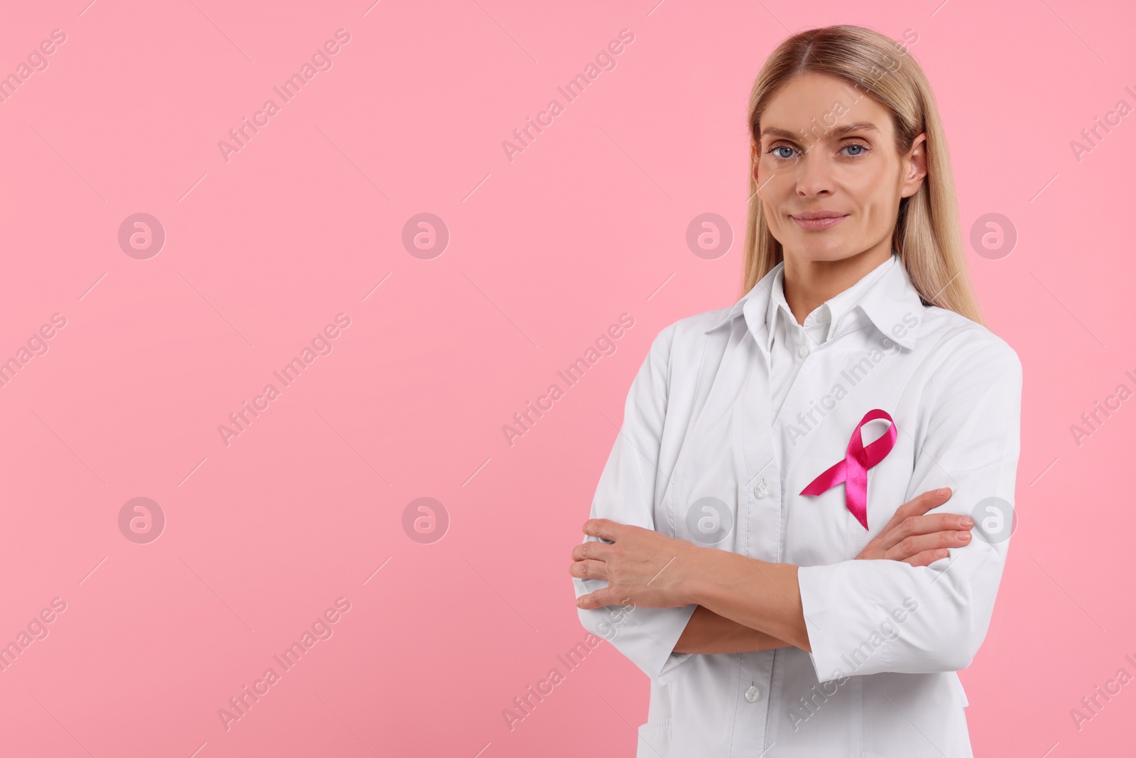 Photo of Doctor with pink ribbon on color background, space for text. Breast cancer awareness