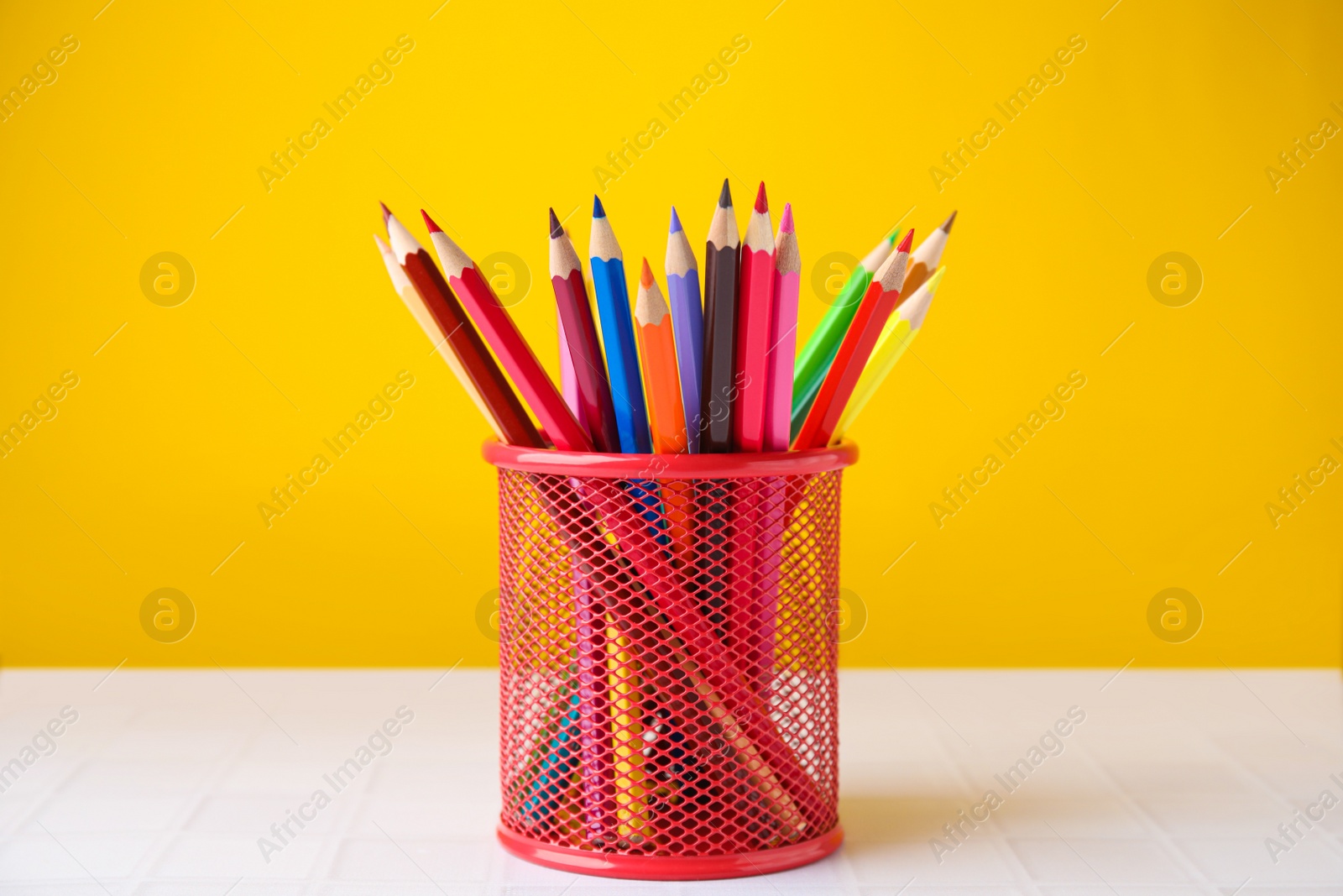 Photo of Many colorful pencils in holder on light table against yellow background