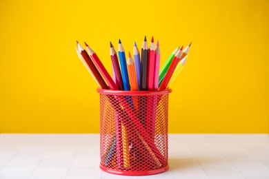 Many colorful pencils in holder on light table against yellow background