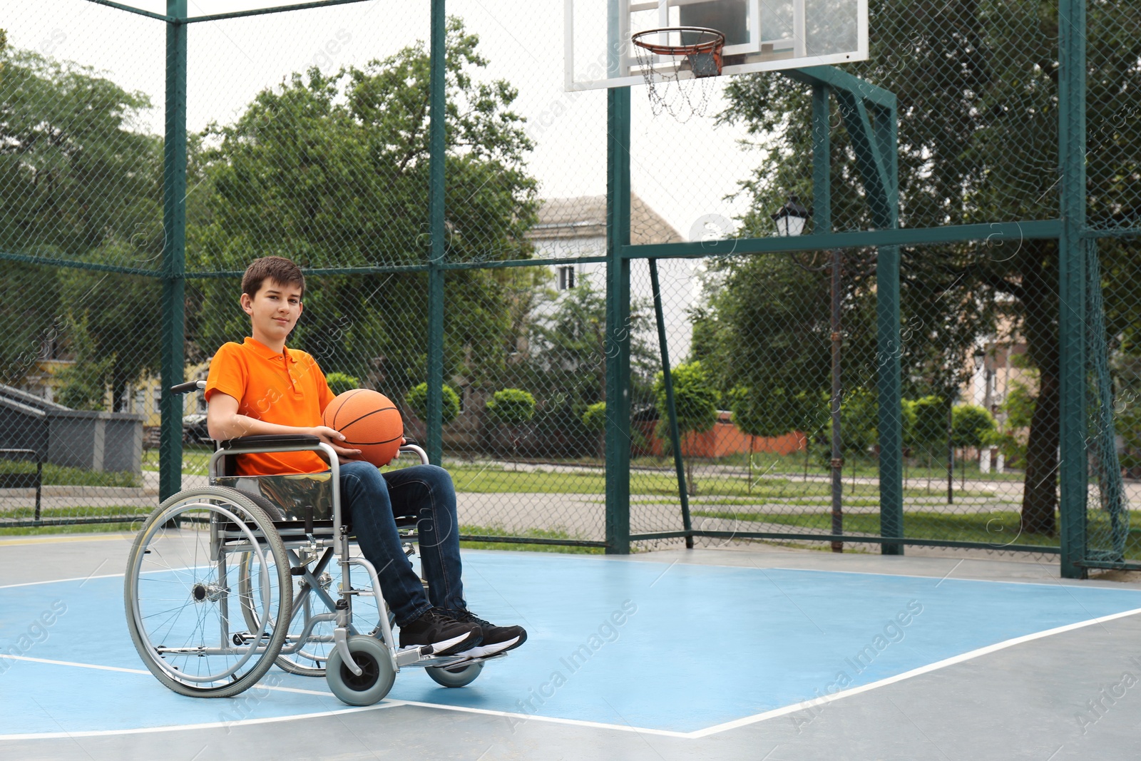 Photo of Disabled teenage boy in wheelchair with basketball ball at outdoor court