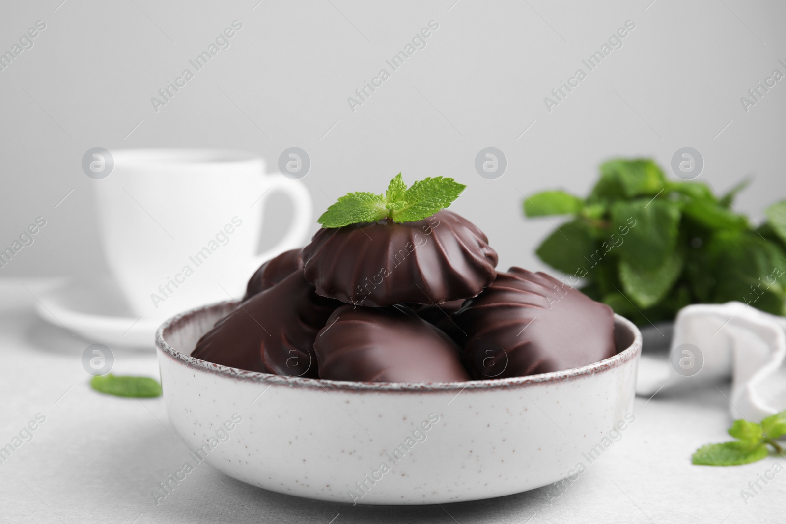 Photo of Delicious chocolate covered zephyrs with mint in bowl on white table
