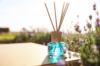 Photo of Reed air freshener on wooden table in blooming lavender field. Space for text
