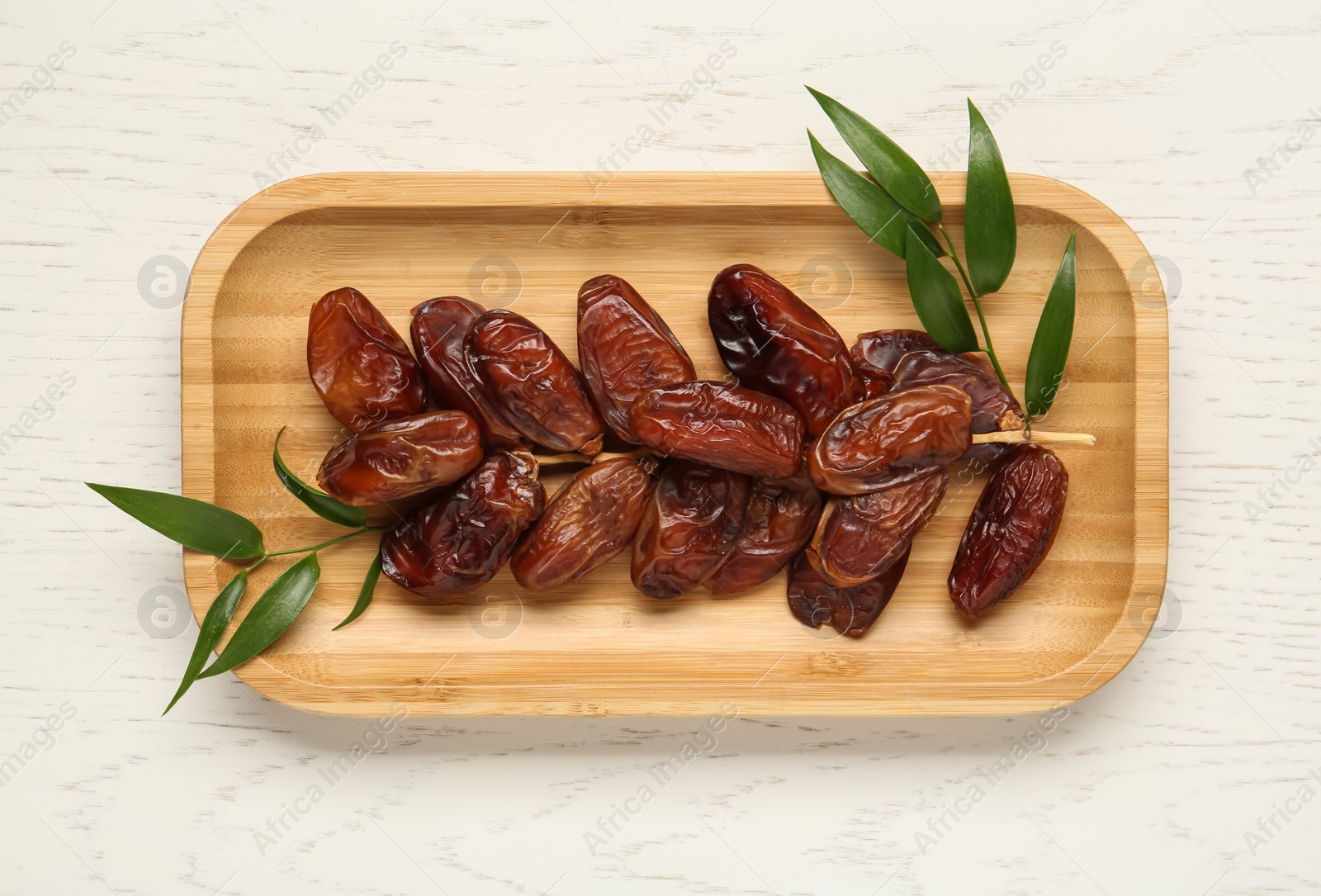 Photo of Plate with sweet dried dates and green leaves on white wooden table, top view