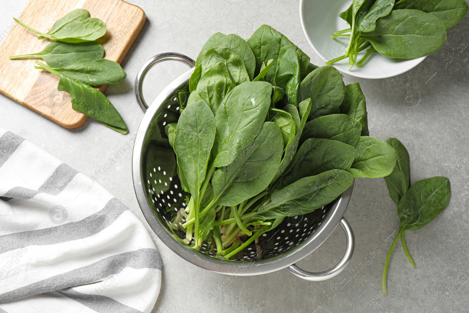 Photo of Colander with fresh green healthy spinach on grey table, flat lay