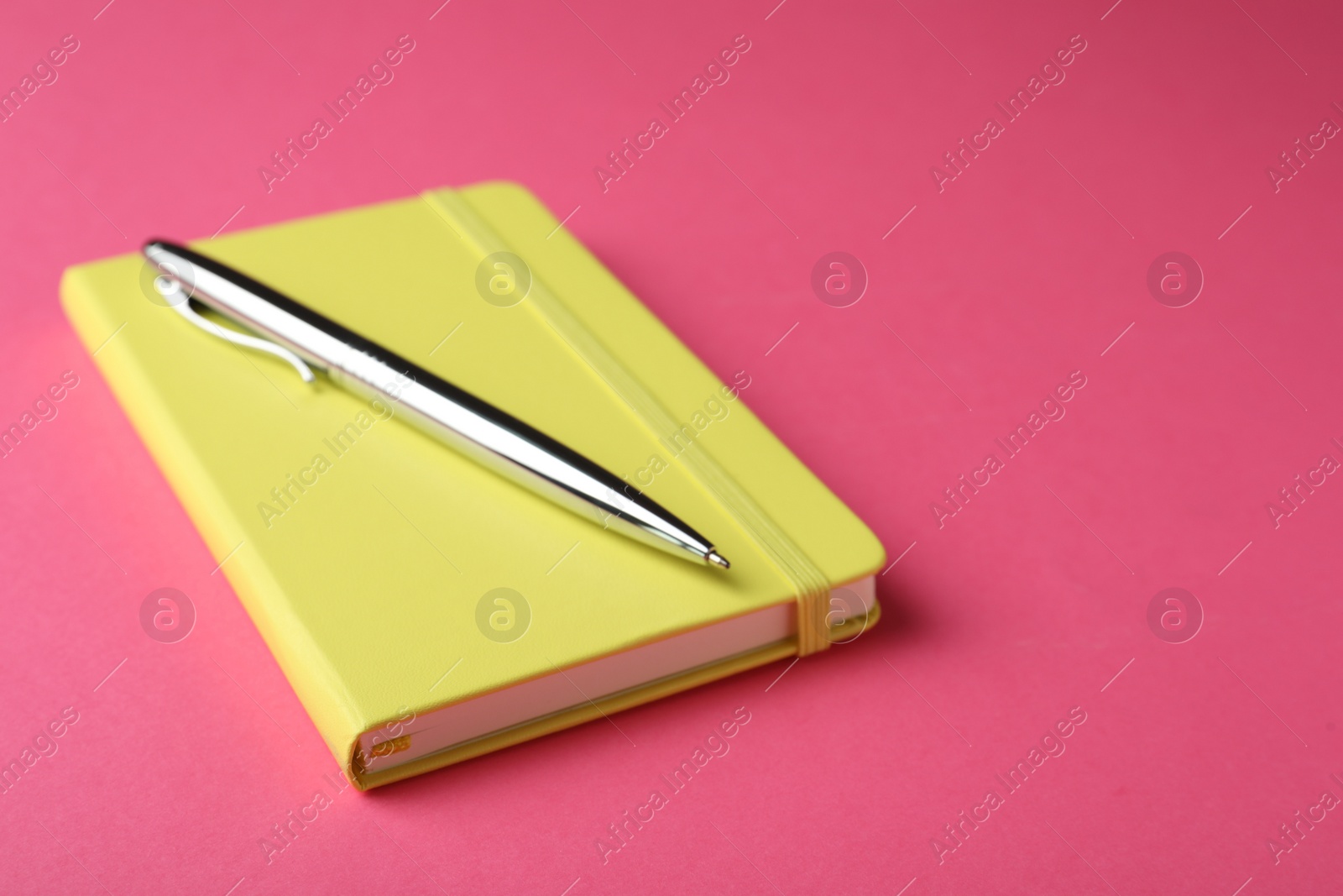 Photo of New stylish planner with hard cover and pen on pink background. Space for text