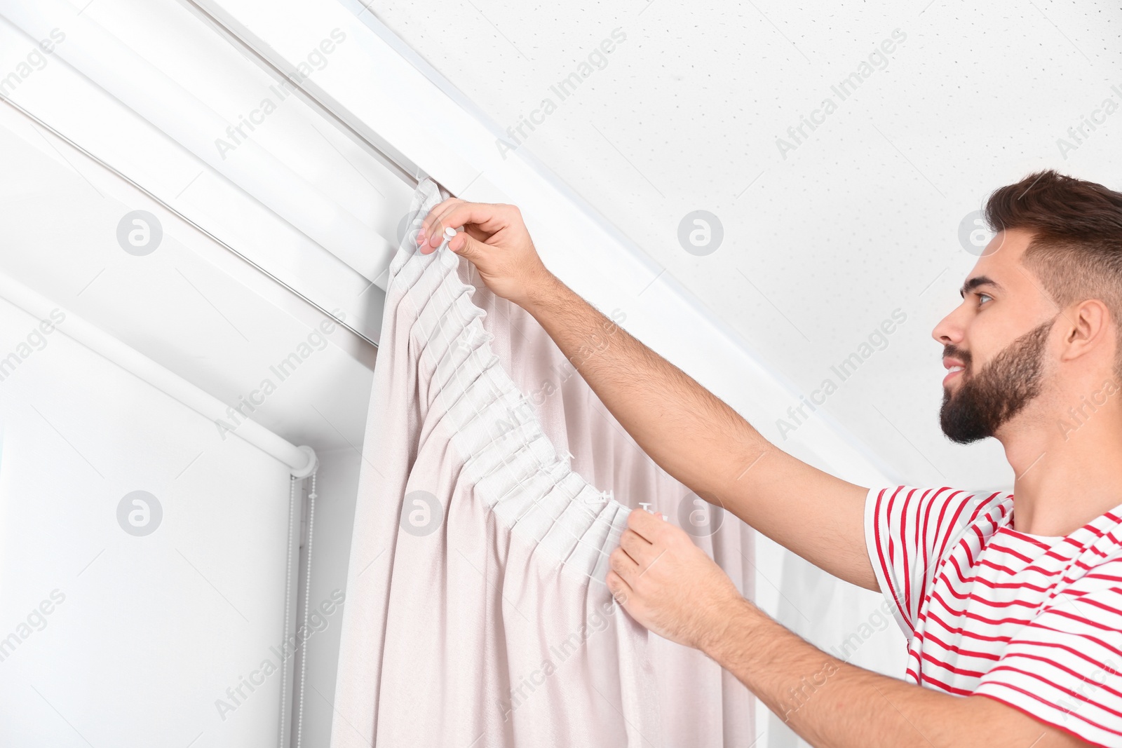 Photo of Young handsome man hanging window curtain in room