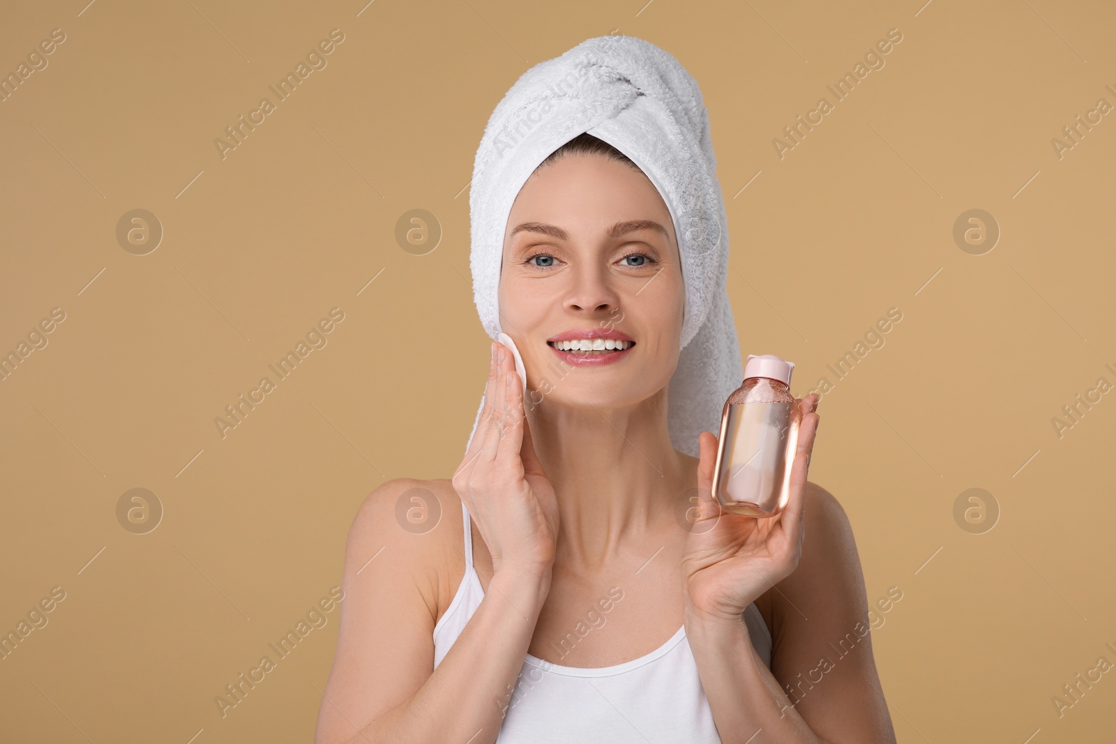 Photo of Beautiful woman in terry towel removing makeup with cotton pad on beige background