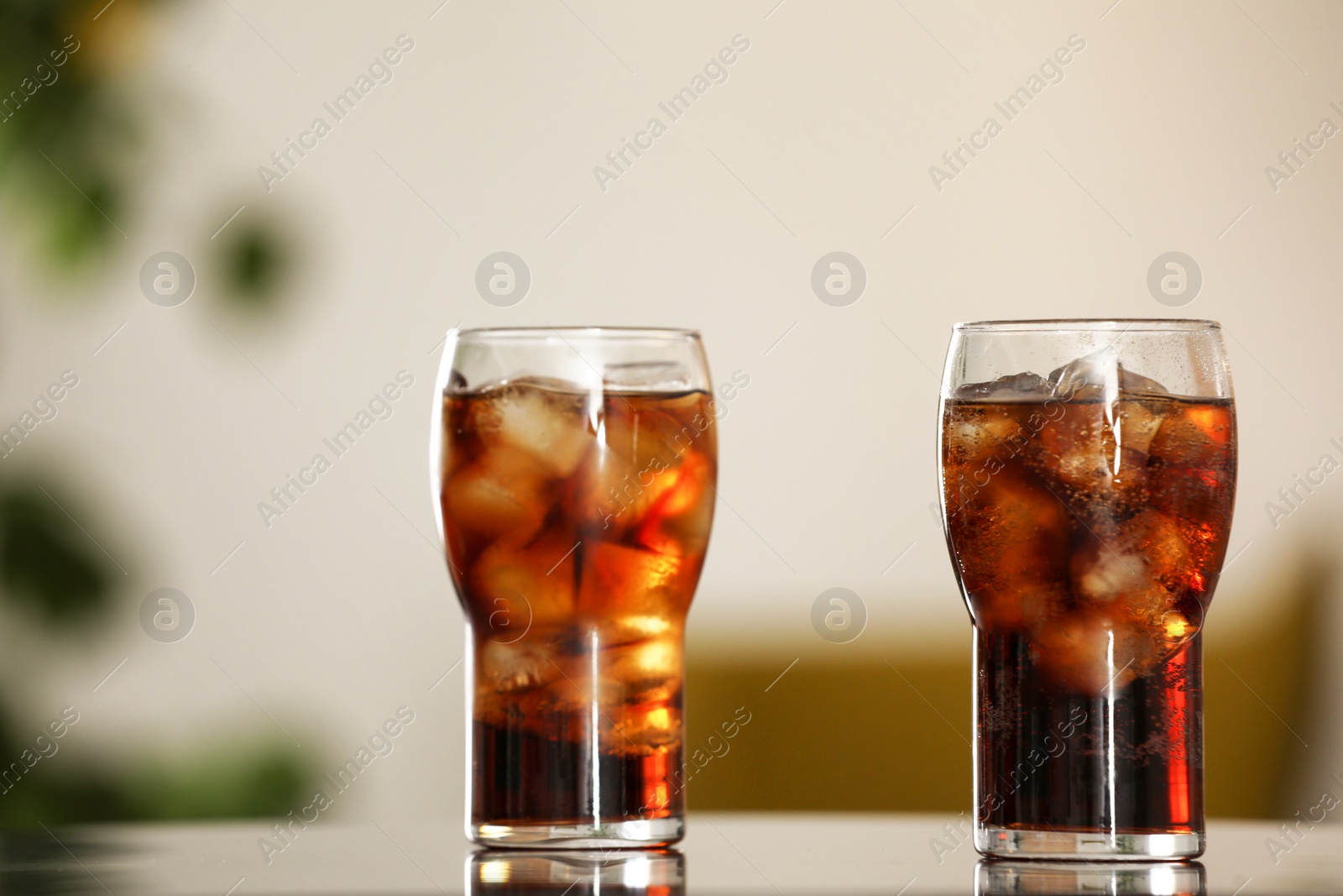 Photo of Glasses of cola with ice on table against blurred background