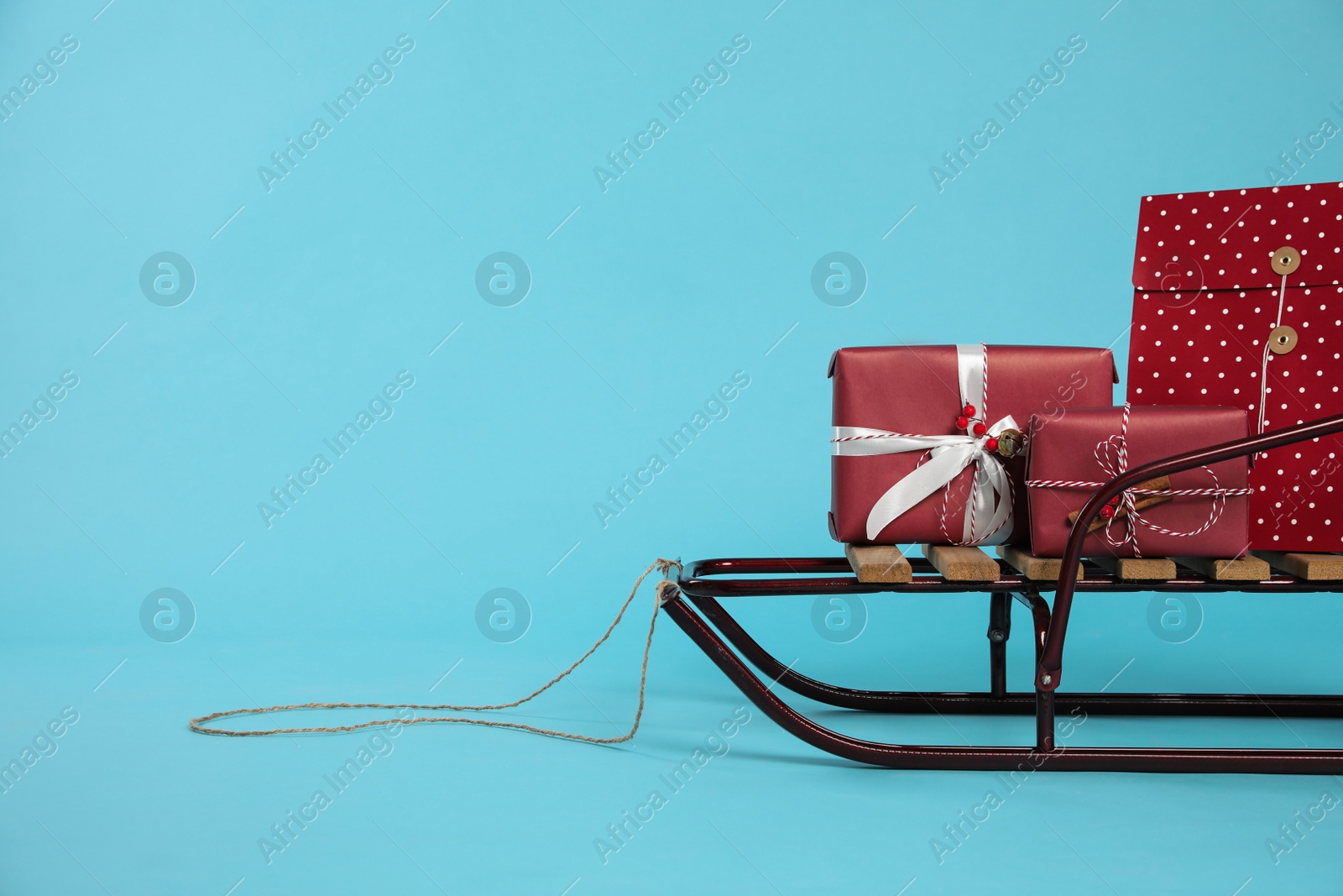 Photo of Stylish sleigh with Christmas gifts on light blue background, space for text