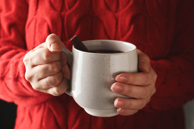 Photo of Woman holding cup of mulled wine with cinnamon, closeup. Winter drink
