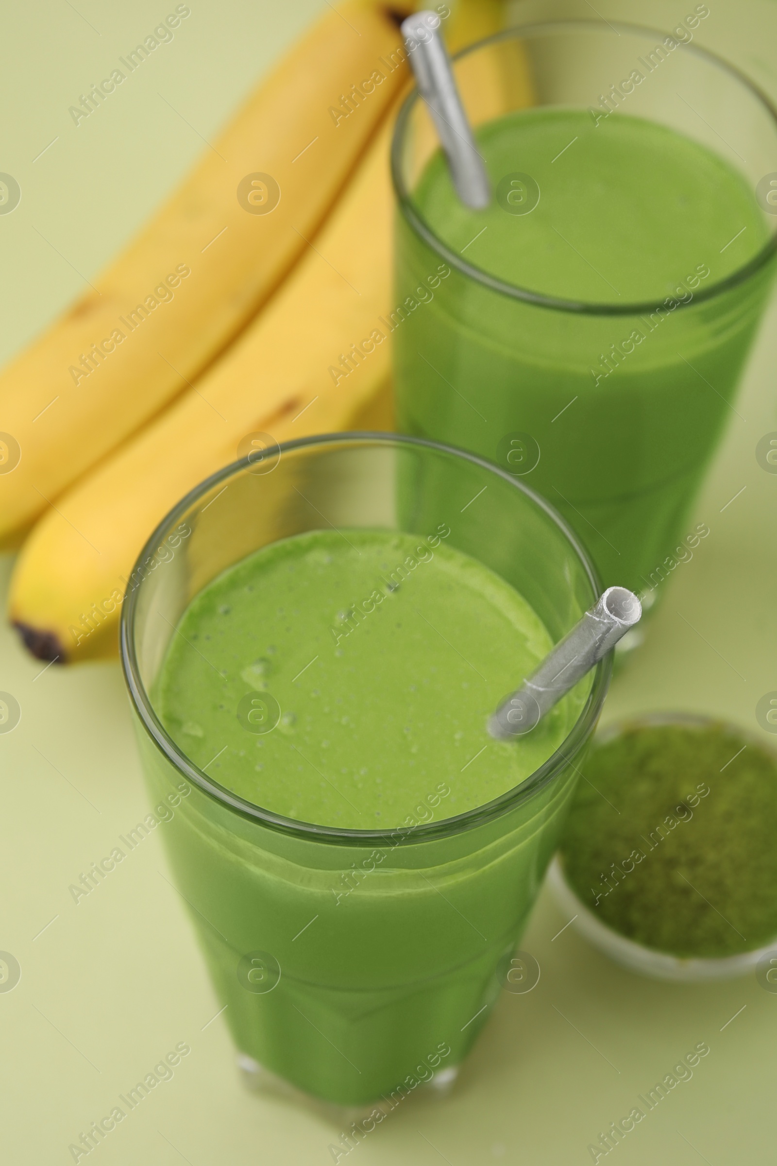 Photo of Glasses of tasty matcha smoothie and powder on pale green background, closeup