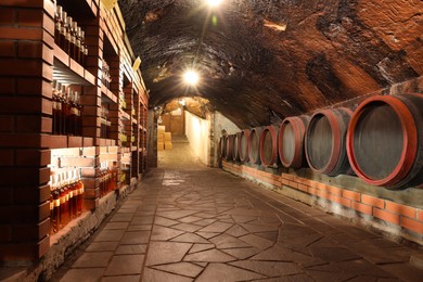 Photo of Many barrels and bottles of wine stored on shelves in cellar