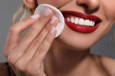 Photo of Smiling woman removing makeup with cotton pad on grey background, closeup