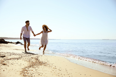 Photo of Happy young couple running on beach near sea. Honeymoon trip