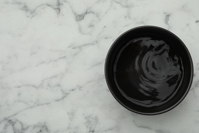 Photo of Black bowl with water on white marble table, top view. Space for text
