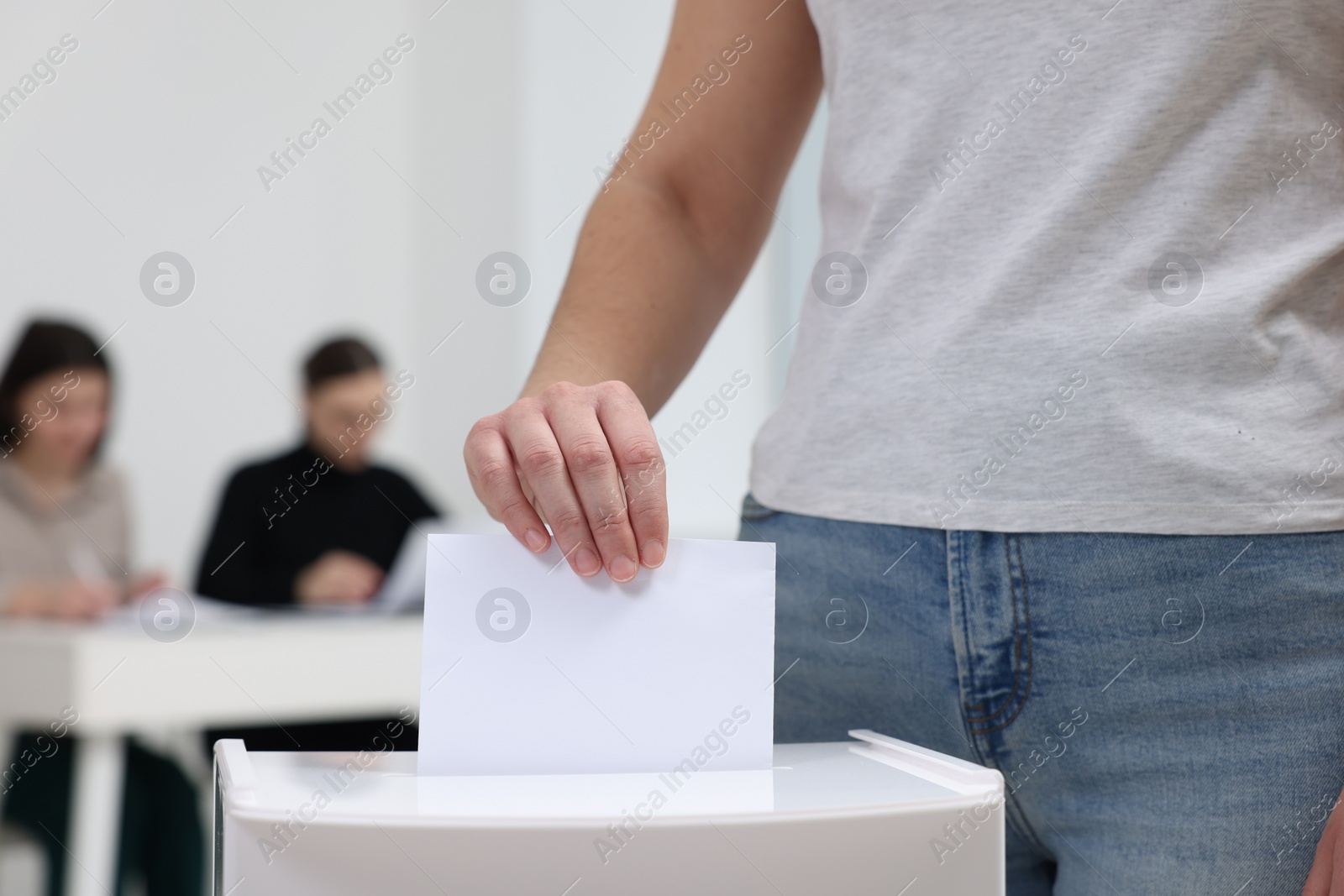 Photo of Woman putting her vote into ballot box on blurred background, closeup