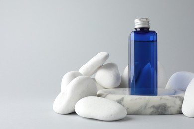 Photo of Bottle of cosmetic product and stones on light grey background. Space for text