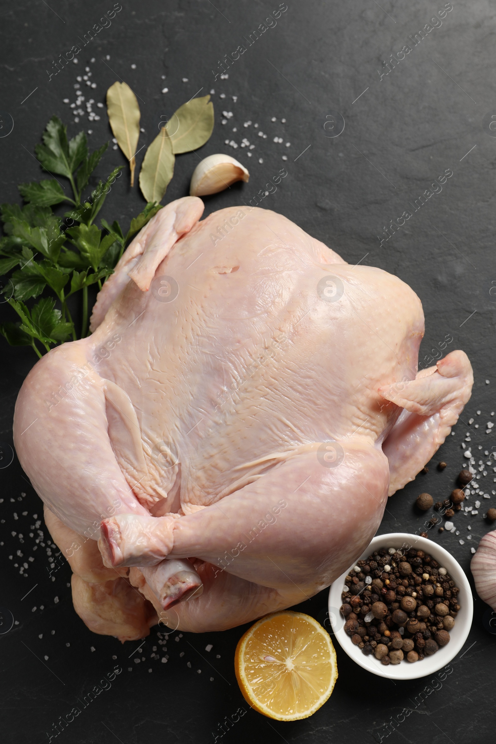 Photo of Fresh raw chicken with spices and lemon on black textured table, flat lay