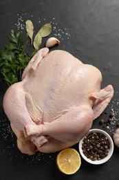 Fresh raw chicken with spices and lemon on black textured table, flat lay