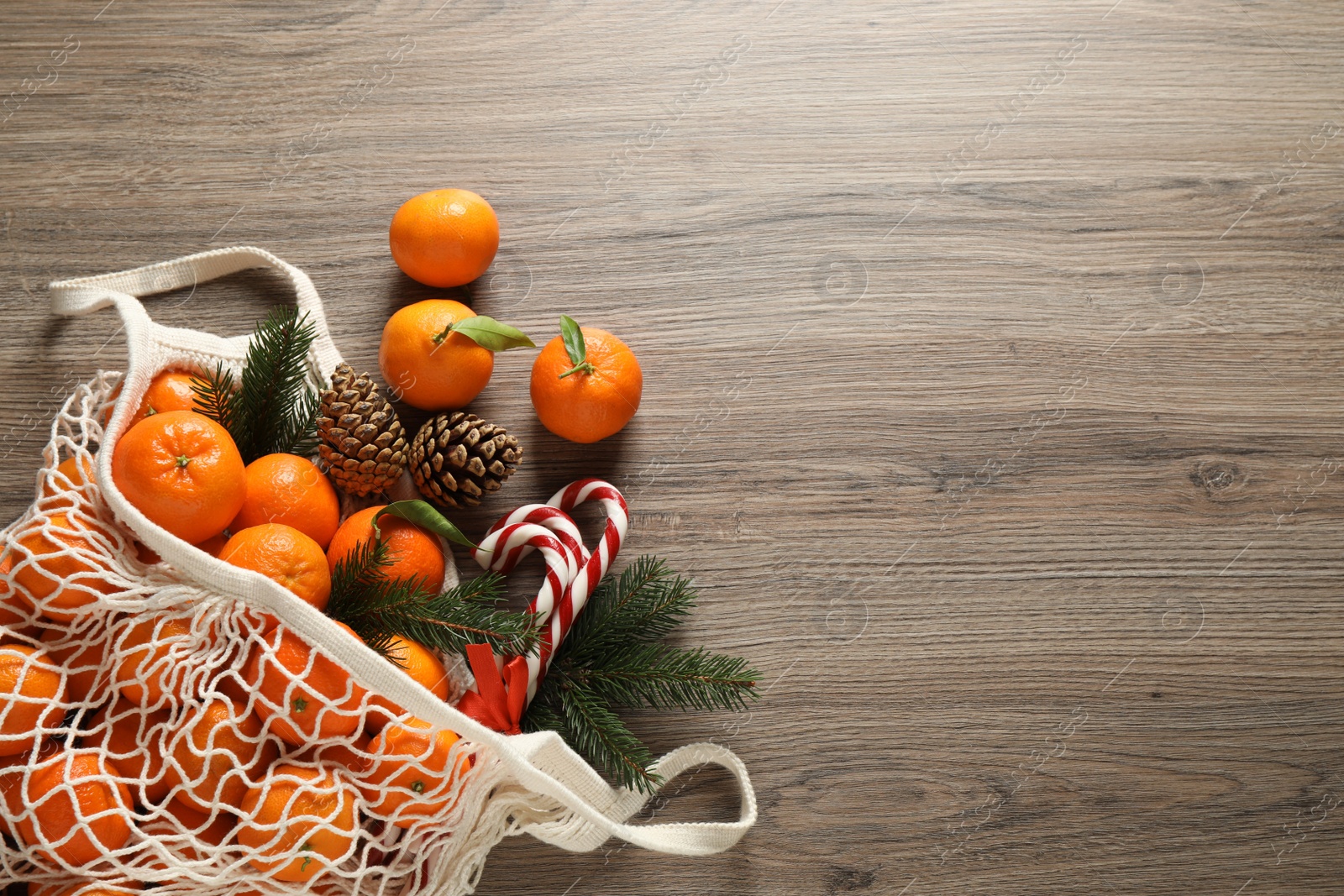 Photo of Flat lay Christmas composition with fresh tangerines in mesh bag on wooden table. Space for text