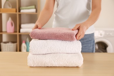 Woman with folded clean terry towels at table in laundry room, closeup