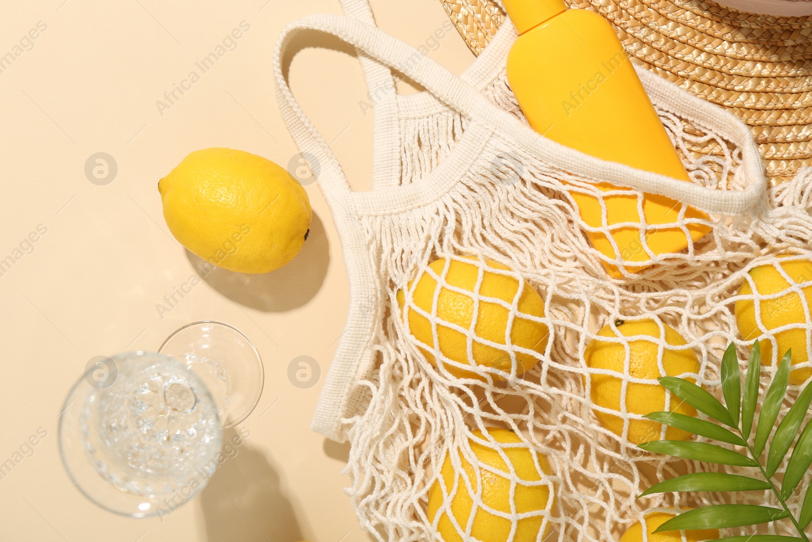 Photo of Fresh lemons, beach accessories in string bag and glass of drink on beige background, flat lay