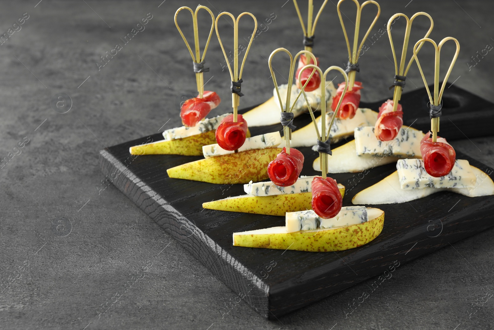 Photo of Tasty canapes with pears, blue cheese and prosciutto on grey table, closeup