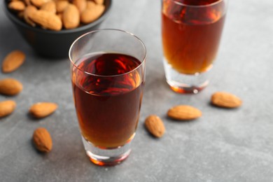 Glasses with tasty amaretto liqueur and almonds on gray table, closeup