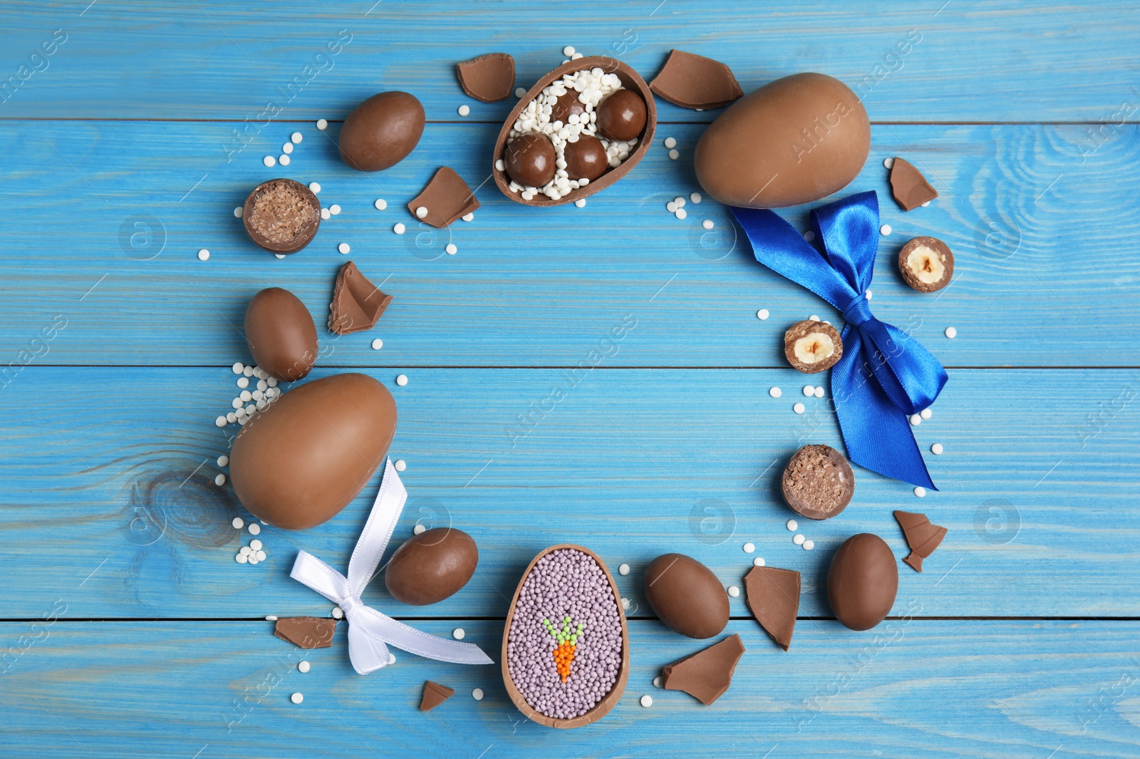 Photo of Frame of chocolate eggs and candies on blue wooden table, flat lay. Space for text