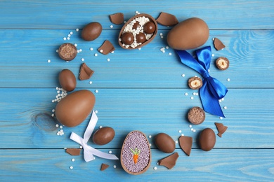 Photo of Frame of chocolate eggs and candies on blue wooden table, flat lay. Space for text