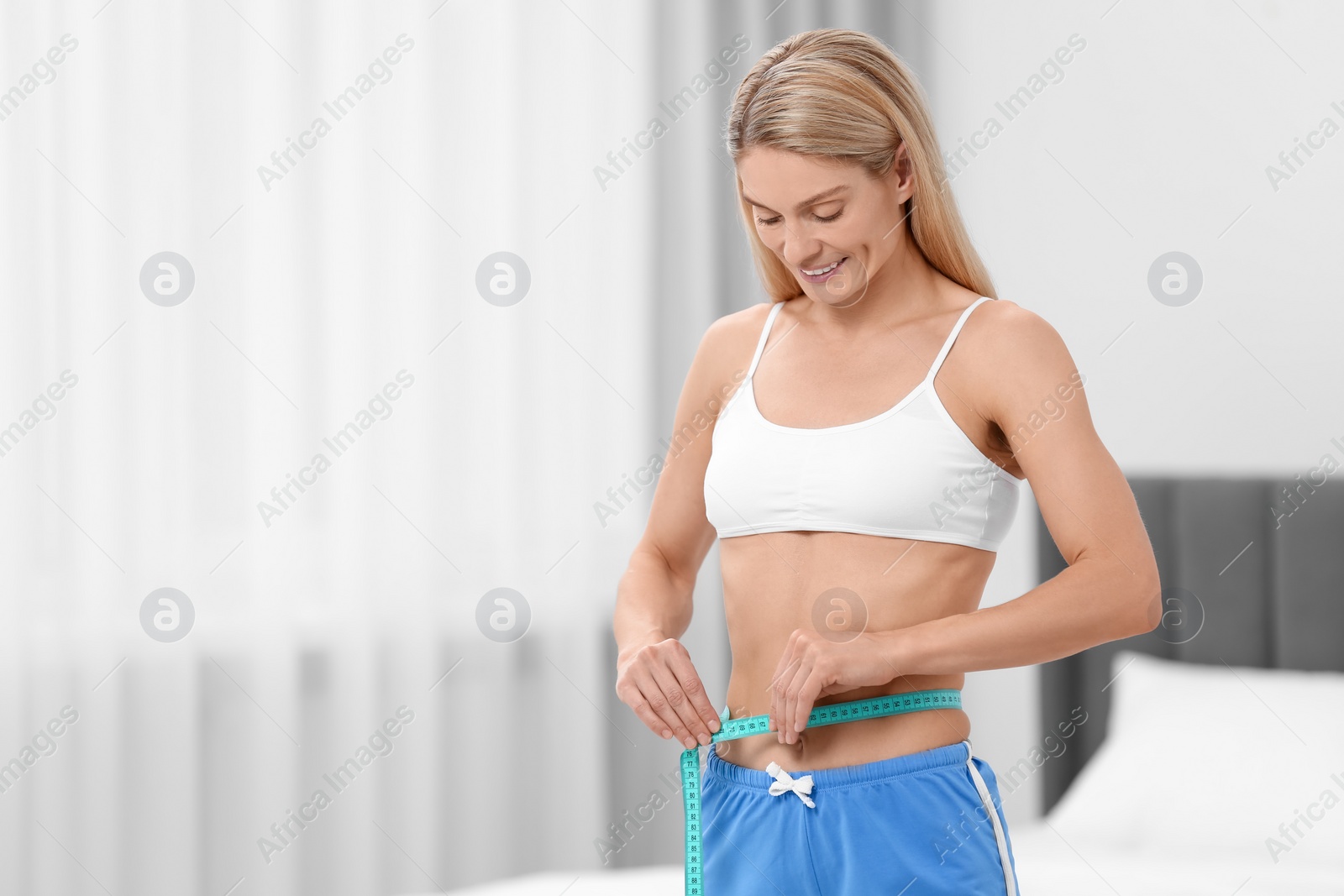 Photo of Slim woman measuring waist with tape at home, space for text. Weight loss