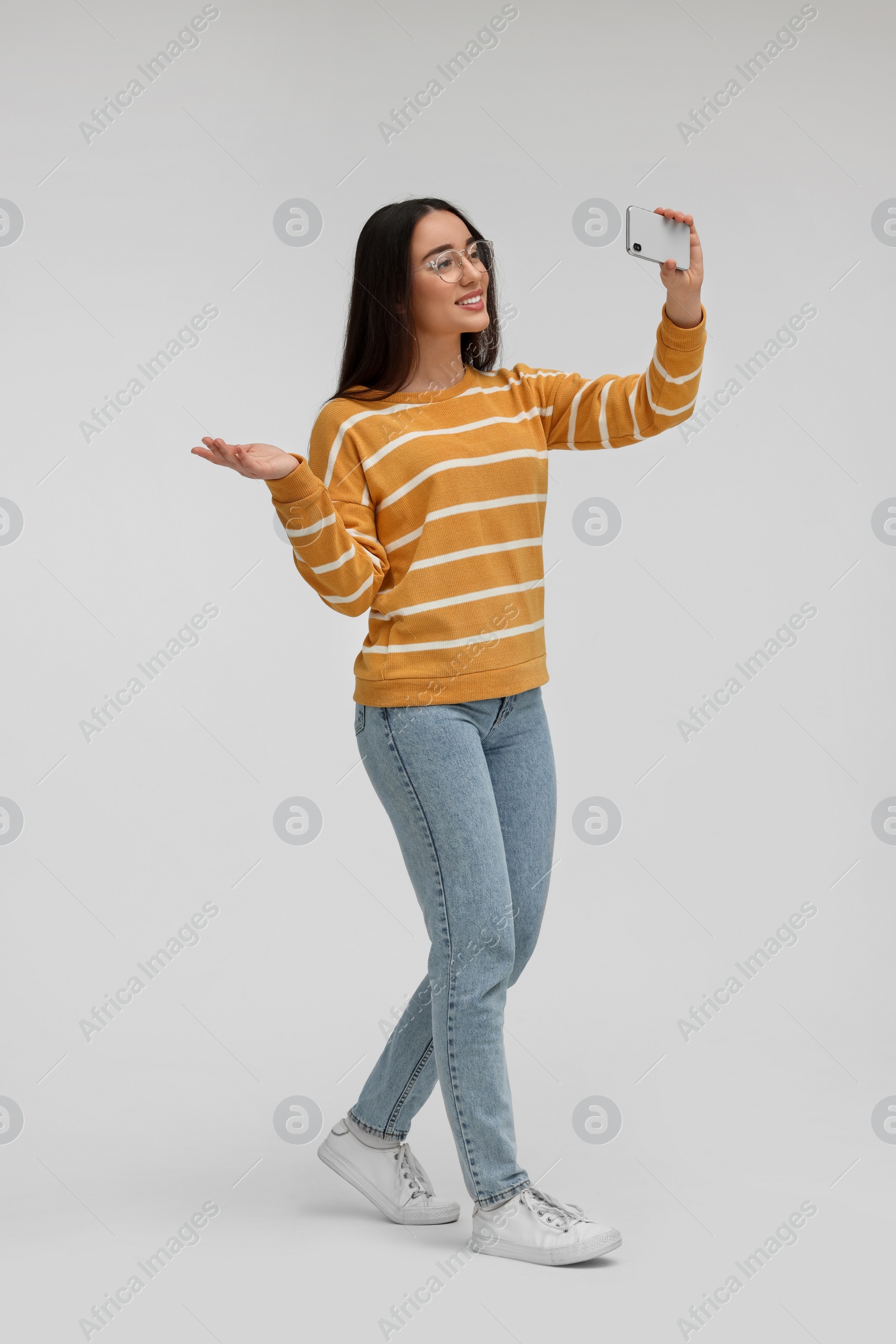 Photo of Smiling young woman taking selfie with smartphone on white background