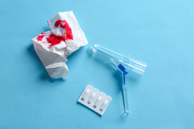 Photo of Anoscope, suppositories and toilet paper with blood on light blue background, flat lay. Hemorrhoid treatment