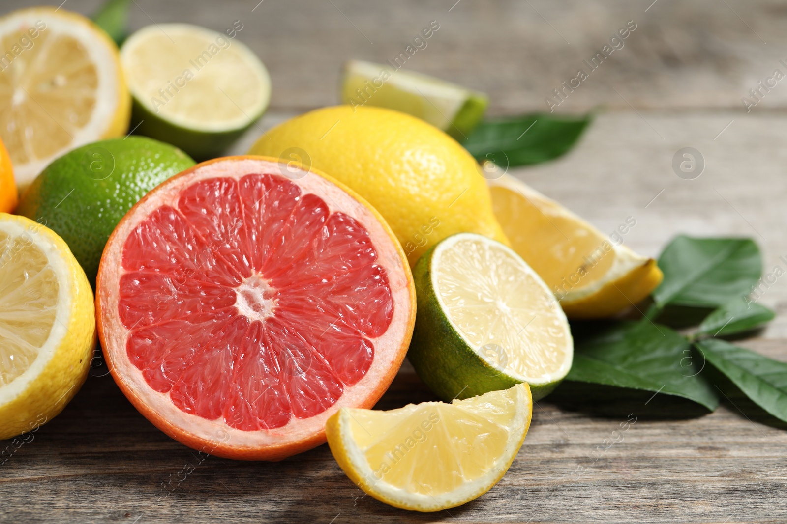 Photo of Different fresh citrus fruits and leaves on wooden table, closeup