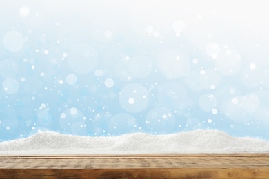 Image of Wooden surface with snow against light blue background, bokeh effect
