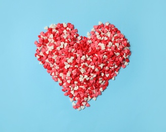 Heart made of bright sprinkles on light blue background, top view