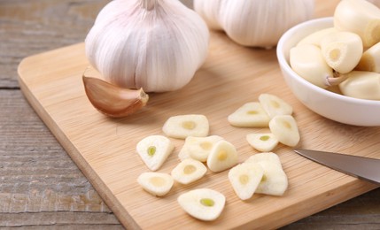 Photo of Aromatic cut garlic, cloves and bulbs on wooden table, closeup