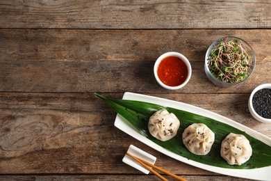 Photo of Flat lay composition with plate of tasty baozi dumplings, sesame seeds, sprouts and sauce on wooden table. Space for text