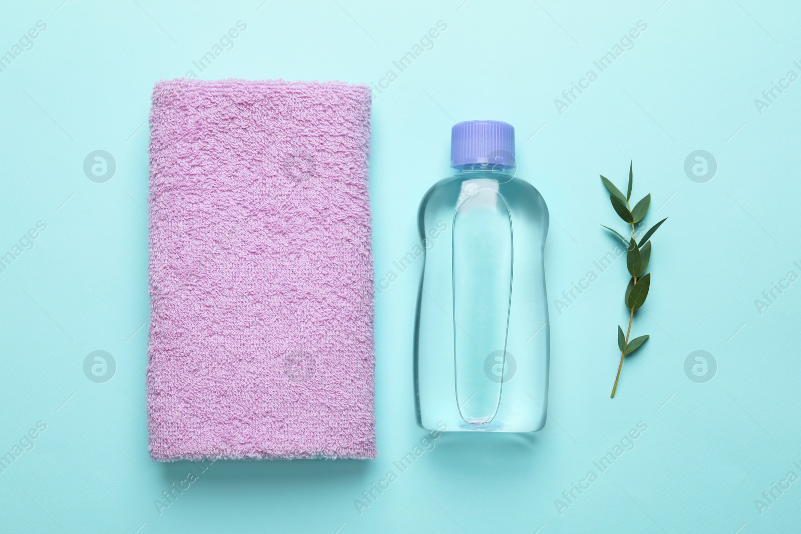 Photo of Bottle of baby oil, towel and leaves on turquoise background, flat lay